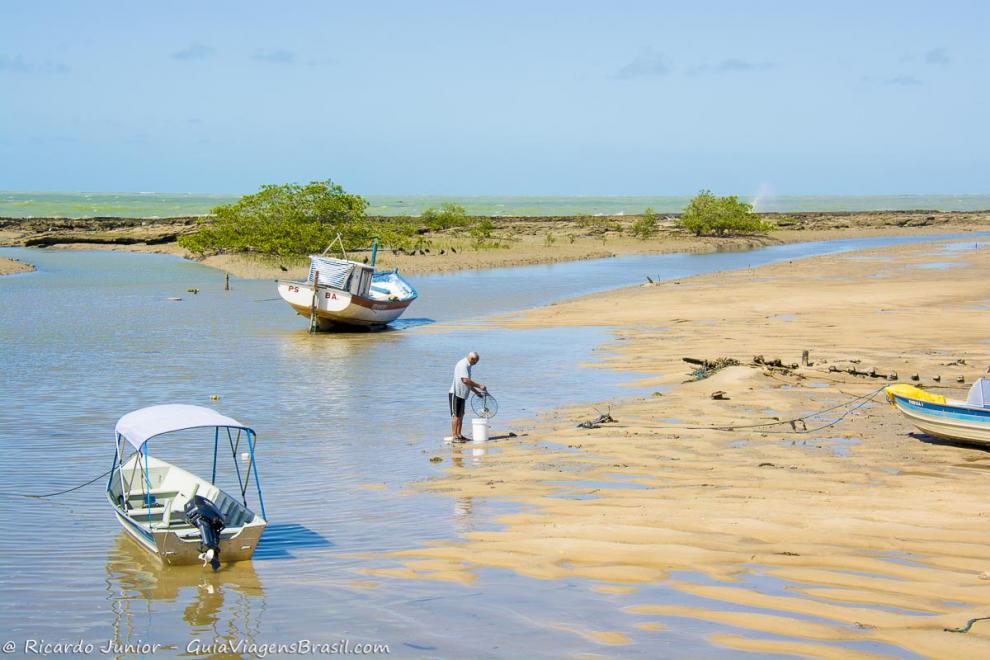 Imagem de um pescador e barcos na piscina natural-Coroa Vermelha.